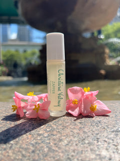 Christine Valmy's all-natural Zapper for oily and breakout-prone skin surrounded by pink flowers. Small, clear, and glass rollerball tube. 